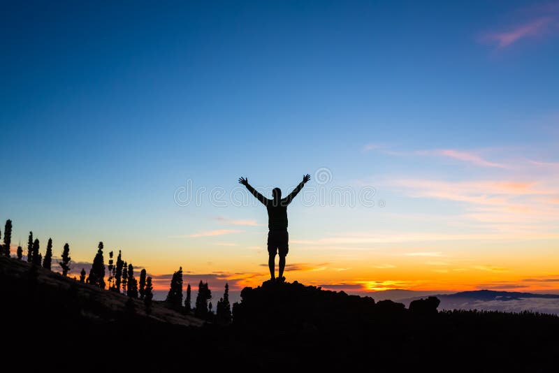 Man celebrating sunset with arms outstretched in mountains. Trail runner, hiker or climber with hands raised reached top of a mountain, enjoy inspirational landscape on Tenerife, Canary Islands