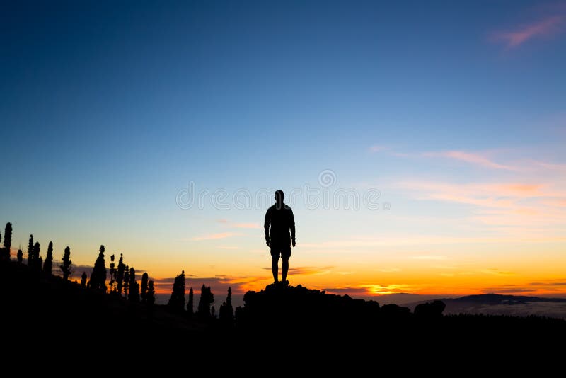 Man celebrating sunset looking at view in mountains. Trail runner, hiker or climber reached top of a mountain, enjoy inspirational landscape on rocky trail on Tenerife, Canary Islands
