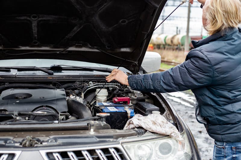 A Man Checks the Oil Level in a Car Engine with an Iron Dipstick