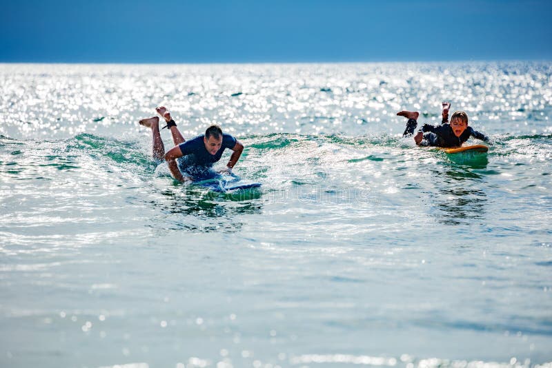Man and a Child Paddling in the Sea To Catch Wave on Surfboard Stock