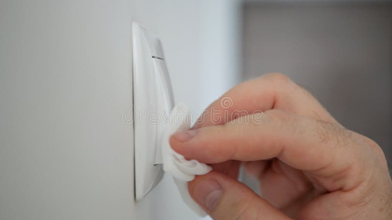 Man Cleaning and Disinfecting Light Switch with Disinfectant and a Clean Wipes