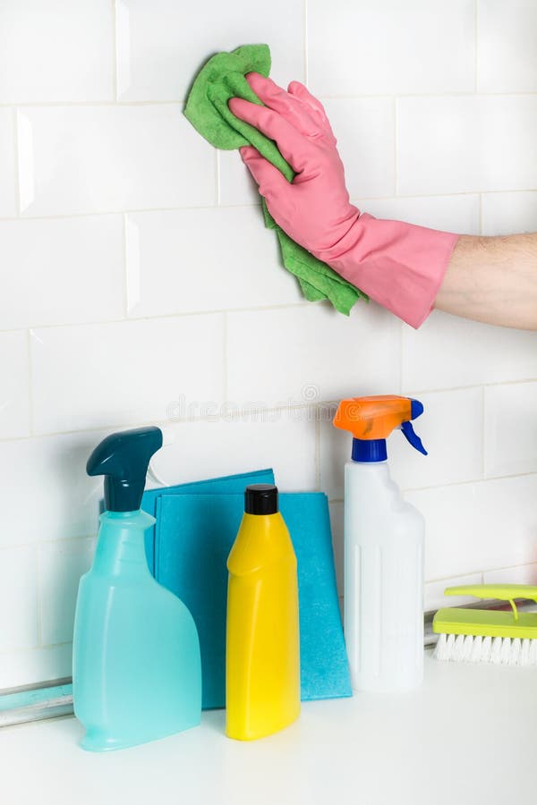 Man cleaning a wall of white subway tiles with a sponge cloth.