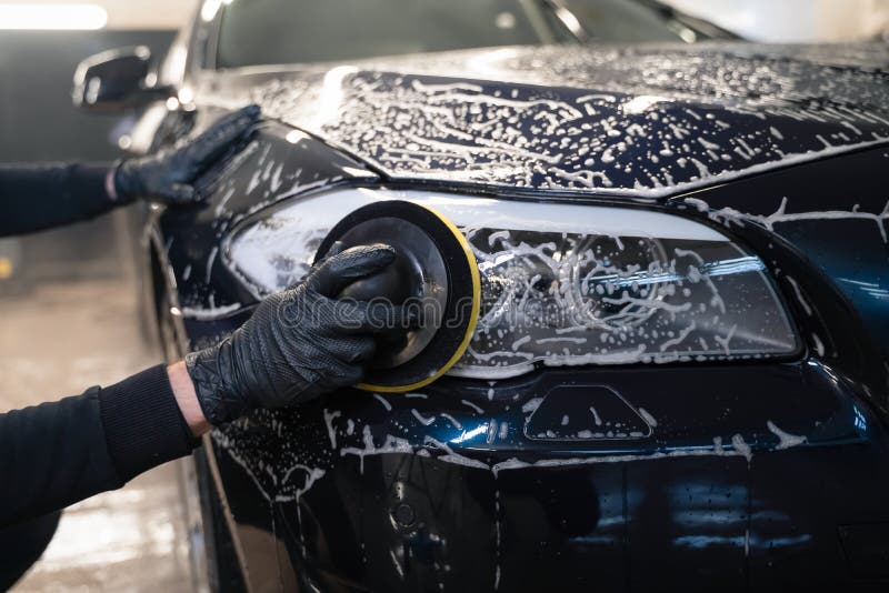 Man cleans car lamp with circle sponge. Preparing auto for polishing. .Detailed car wash.