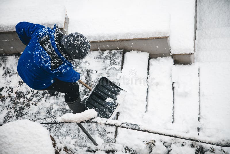 Man is clearing the snow on staircases, snow pusher and shovelling