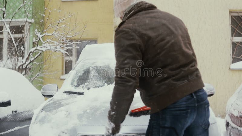 Man clears snow from his car on the street in winter, front view, time lapse