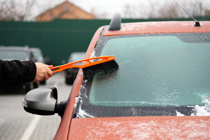 Man Clears Snow from Icy Windows of Car. Brush in Mans Hand. Windshield