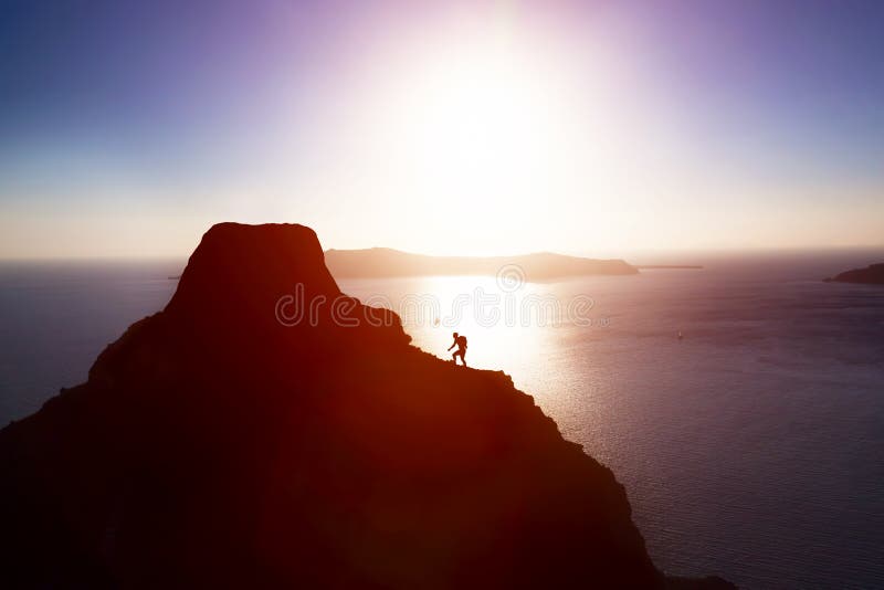 Man climbing up hill to reach the peak of the mountain over ocean.