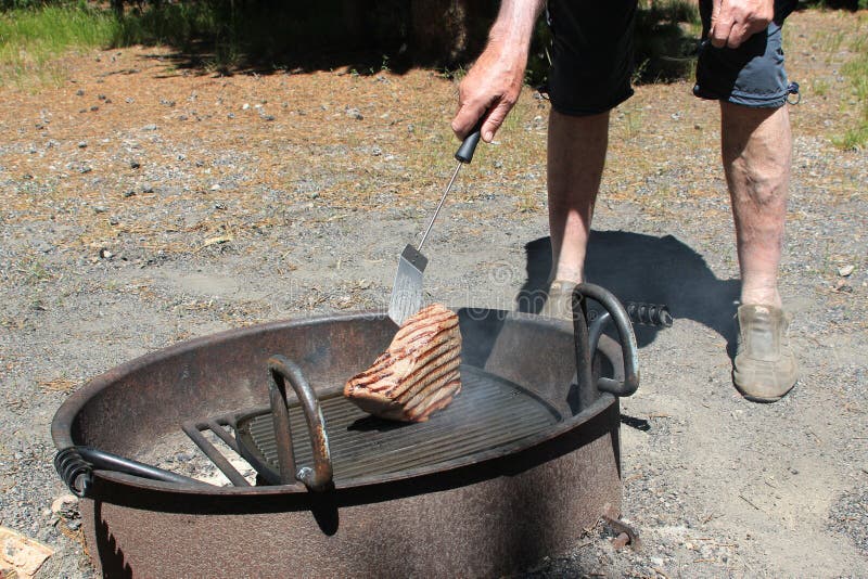 Man Cooking A Large Steak On A BBQ Grill Over A Fire Pit ...