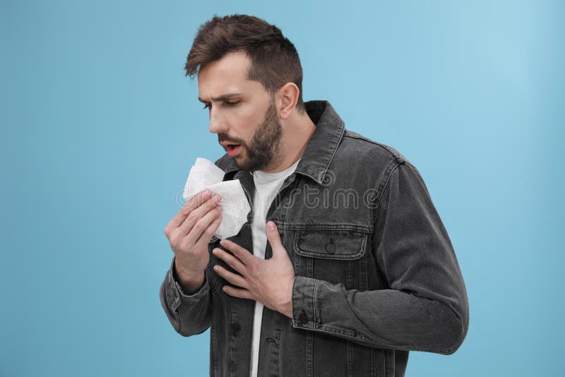 Man Coughing on Light Blue Background. Cold Symptoms Stock Photo
