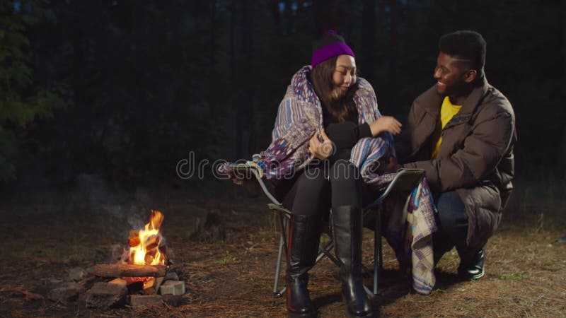 Man covering cold woman with blanket in camping