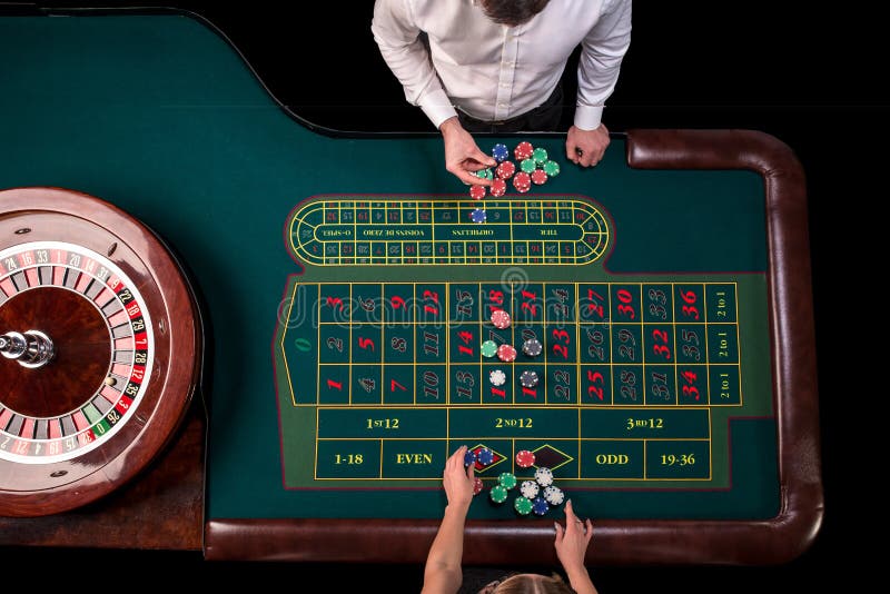 Man croupier och kvinnan som spelar rouletten på tabellen i kasinot Bästa sikt på en grön tabell för roulett med ett band arkivbilder Man croupier och kvinnan som spelar rouletten på tabellen i kasinot Bästa sikt på en grön tabell för roulett med ett band arkivbilder