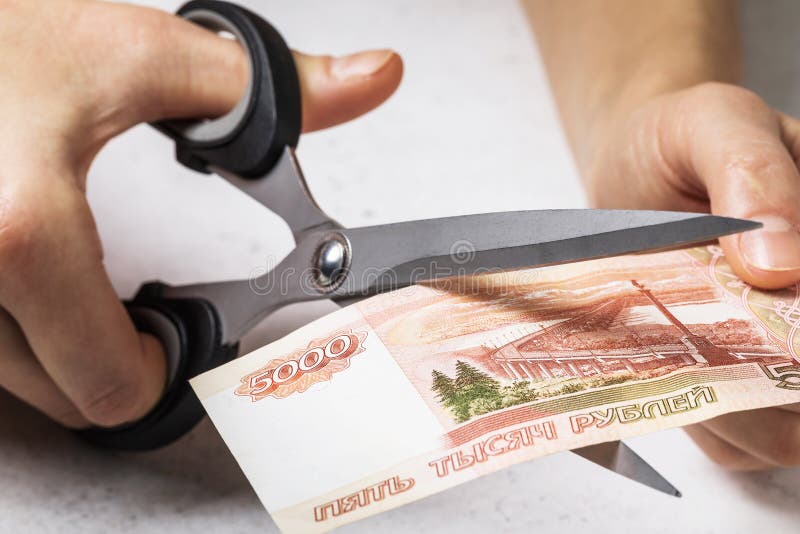 A man cuts with scissors five thousand Russian rubles. The concept of the depreciation of money in the country