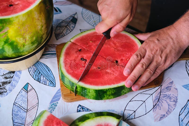 A man cuts a watermelon circle into triangular segments on a board on a plastic-covered table. Snack. Triangular cut watermelon stock images, royalty-free photos and pictures