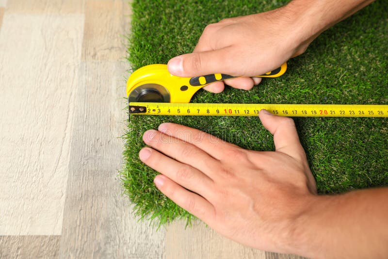 Man cutting artificial grass carpet indoors, closeup.