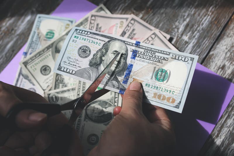 Man is cutting dollar banknotes with scissors on the purple pastel background. Money notes on the wooden  surface. Devaluation of