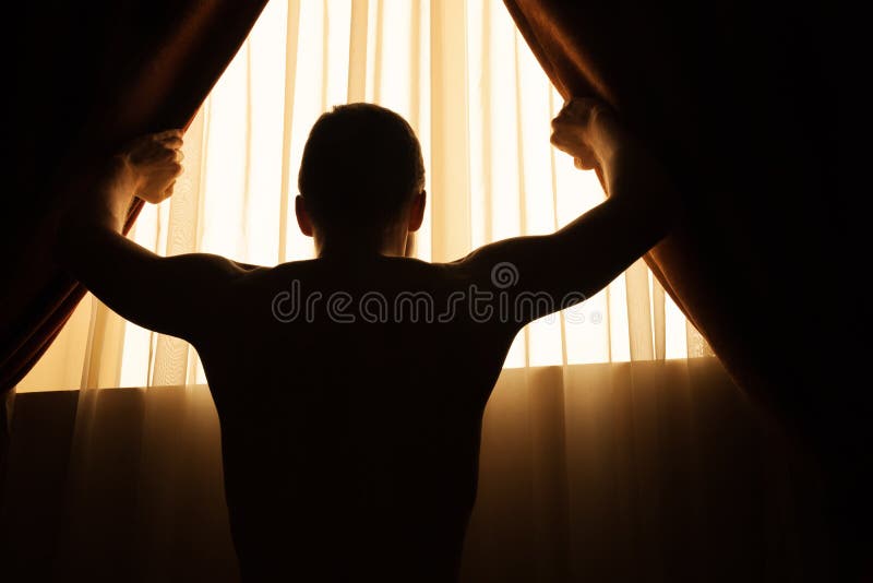 Man in dark room opens curtains on window