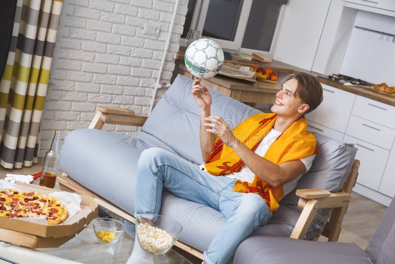 Man den hållande ögonen på sporten på ensamt spela för tv hemma med bollen royaltyfri foto Man den hållande ögonen på sporten på ensamt spela för tv hemma med bollen royaltyfri foto