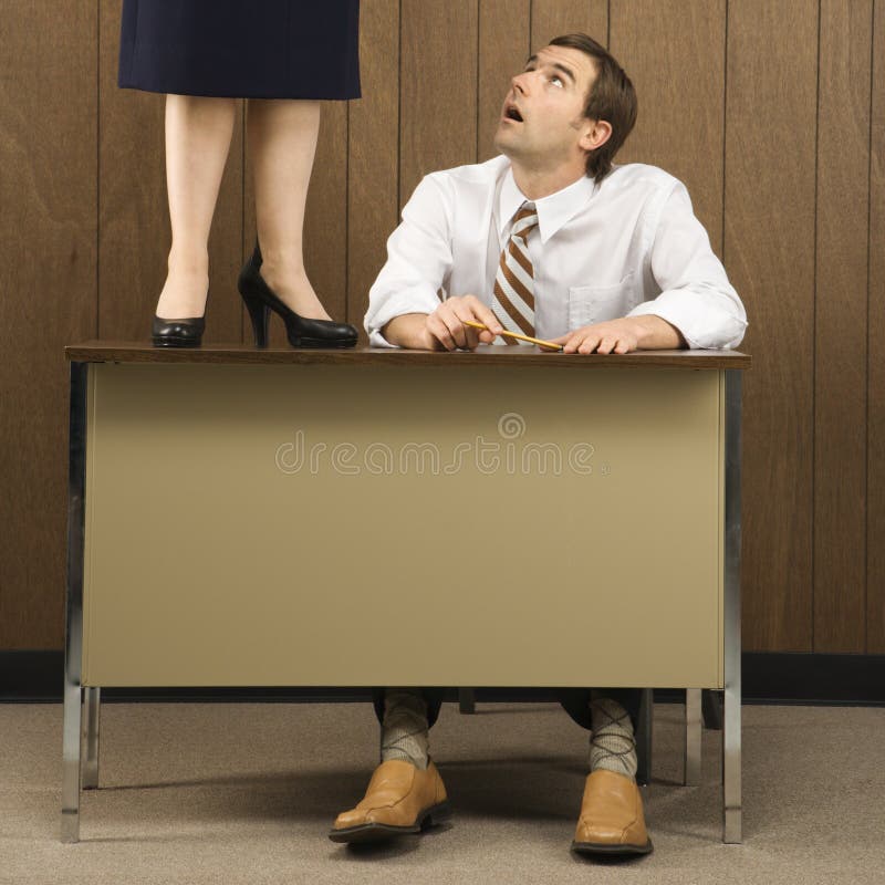 Mid-adult Caucasian male sitting at desk looking up to Caucasian female standing on desk. Mid-adult Caucasian male sitting at desk looking up to Caucasian female standing on desk.