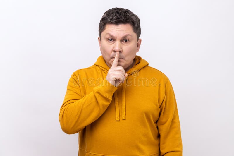 Portrait of middle aged man holding finger on lips making hush silence gesture, asking to keep secret, don&#x27;t speak, wearing urban style hoodie. Indoor studio shot isolated on white background. Portrait of middle aged man holding finger on lips making hush silence gesture, asking to keep secret, don&#x27;t speak, wearing urban style hoodie. Indoor studio shot isolated on white background.