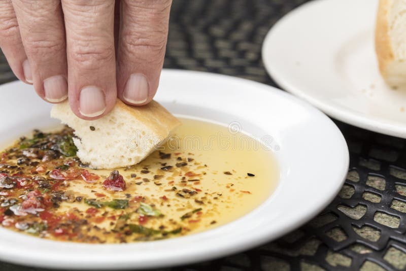 Man dipping bread in a seasoned olive oil on a white plate