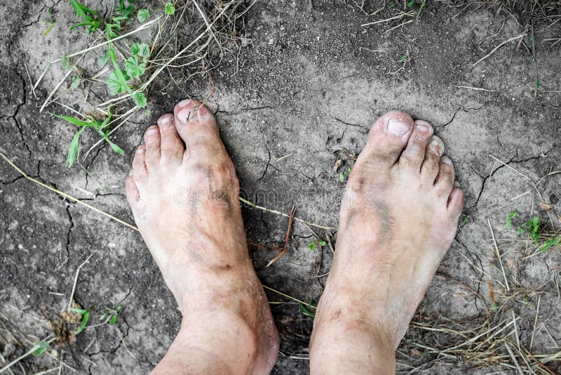 A man with dirty feet stands on the ground cracked from the heat. The concept of poverty