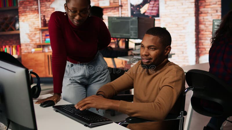 Man with disability typing on PC and chatting with coworker stock video