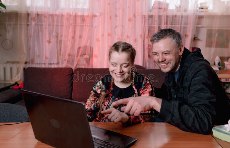 a man and a disabled girl look at their laptop and smile. people with down syndrome