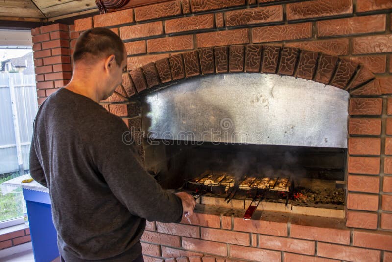 Man Doing Barbecue, Grilling Kebabs on the Fire in the Oven Stock Photo