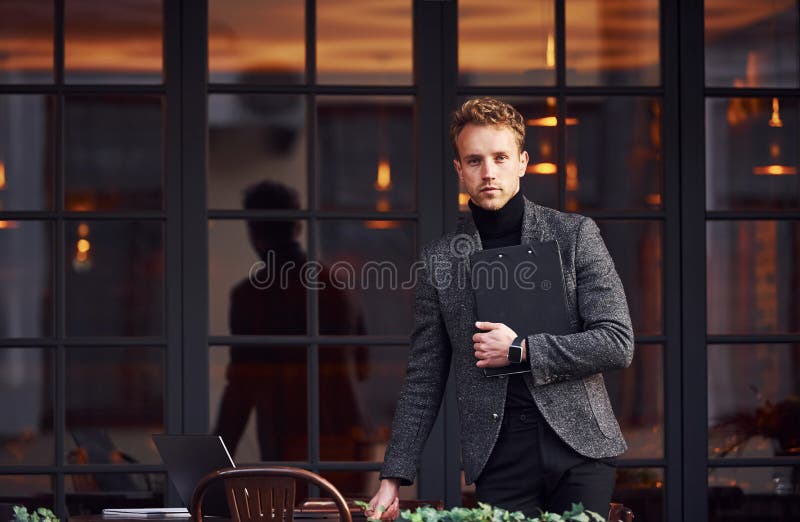 Man in elegant formal wear with cup of drink and notepad in hands