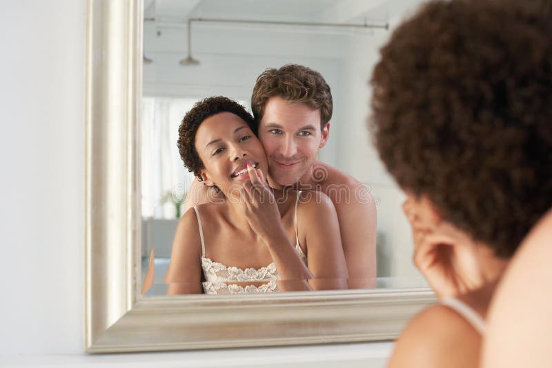 Man Embracing Woman Applying Lipstick In Mirror