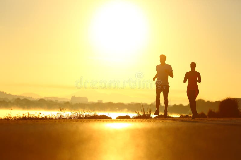Man en vrouwensilhouetten die bij zonsopgang lopen stock foto Man en vrouwensilhouetten die bij zonsopgang lopen stock foto