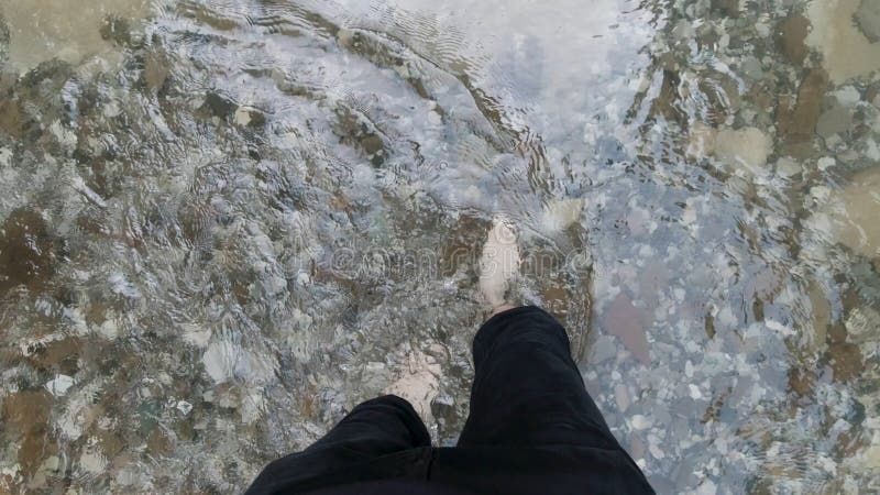 Man feet with hairy legs crossing cold mountain stream. Top view of male bare legs walking through cold river with stony bottom, concept of hiking. Man feet with hairy legs crossing cold mountain stream. Top view of male bare legs walking through cold river with stony bottom, concept of hiking.