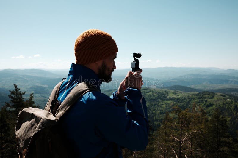 Man filming scenic mountain view with a compact gimbal camera on a sunny spring day in Zlatibor, Serbia. Travel blogger making royalty free stock photography