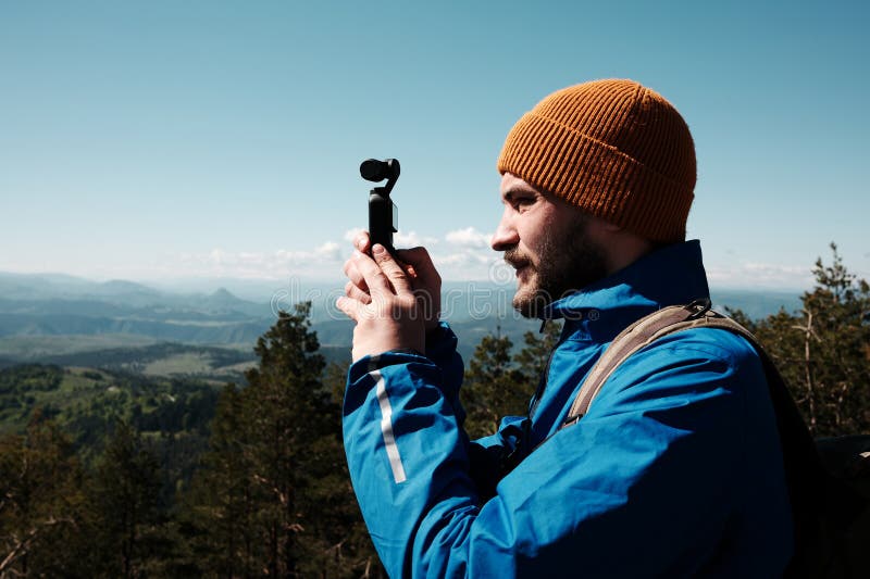 Man filming scenic mountain view with a compact gimbal camera on a sunny spring day in Zlatibor, Serbia. Travel blogger making royalty free stock photos