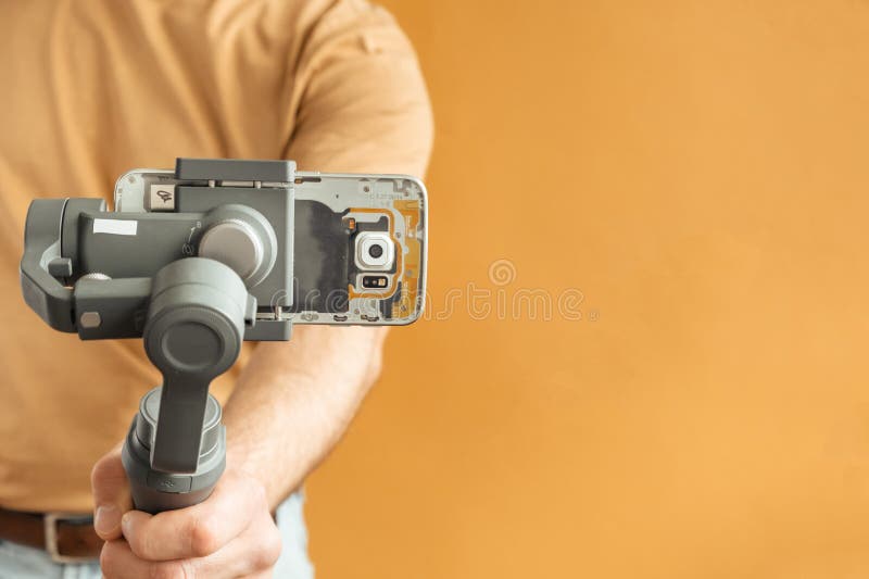 Man filming with a smartphone using a gimbal stabilizer on yellow background. Using three-axis electronic stabilizer to make vlogs stock photo