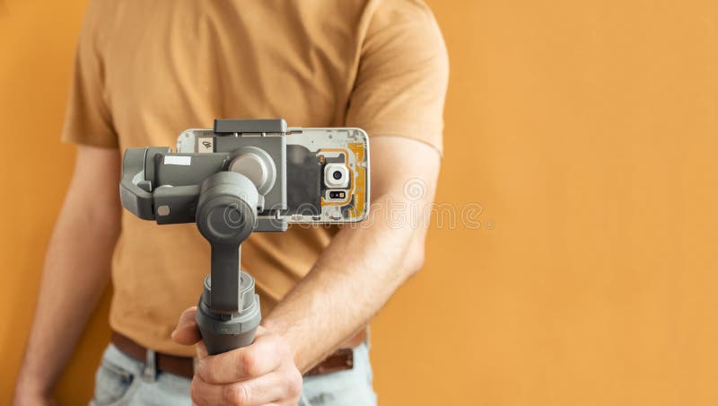Man filming with a smartphone using a gimbal stabilizer on yellow background. Using three-axis electronic stabilizer to make vlogs royalty free stock photos
