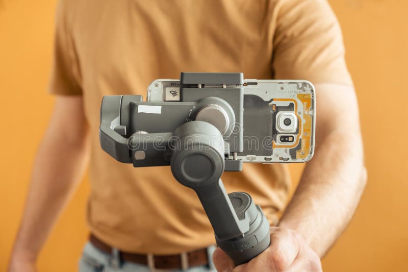 Man filming with a smartphone using a gimbal stabilizer on yellow background. Using three-axis electronic stabilizer to make vlogs royalty free stock photo