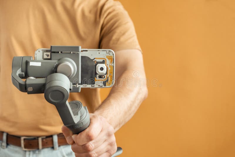 Man filming with a smartphone using a gimbal stabilizer on yellow background. Using three-axis electronic stabilizer to make vlogs royalty free stock image