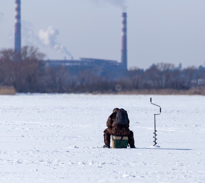 A man fishing with a fishing rod on the ice in winter royalty free stock photo