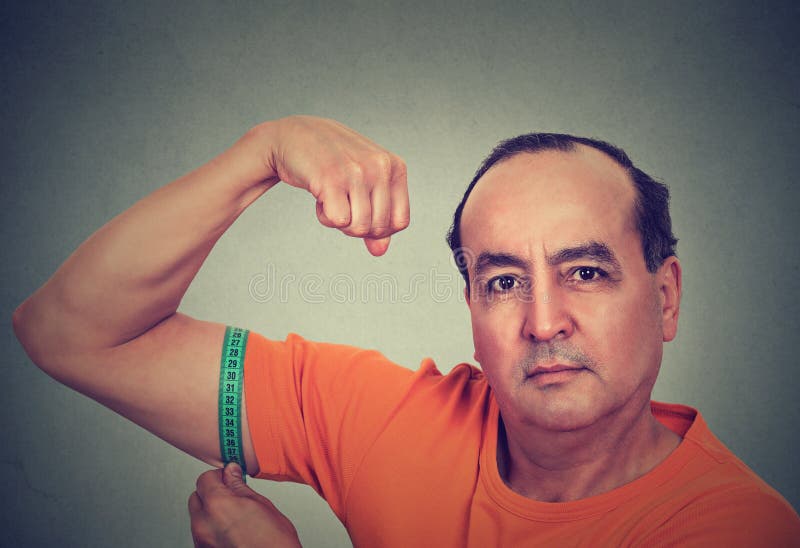 Closeup middle aged man flexing his muscle measuring his biceps isolated on gray wall background. Fitness goal achievement result concept. Closeup middle aged man flexing his muscle measuring his biceps isolated on gray wall background. Fitness goal achievement result concept