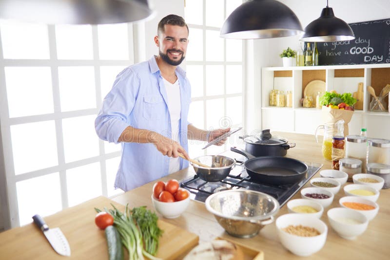 Man following recipe on digital tablet and cooking tasty and healthy food in kitchen at home royalty free stock photography Man following recipe on digital tablet and cooking tasty and healthy food in kitchen at home royalty free stock photography