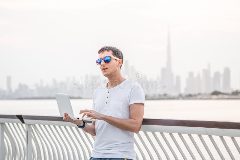 Happy man freelance programmer and junior developer writes code and thinks about a project in the paradise resort city of Dubai against the backdrop of the famous Burj Khalifa skyscraper