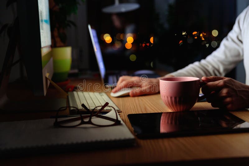 Man freelancer drinking tea while working late at night at computer at home office, remote work