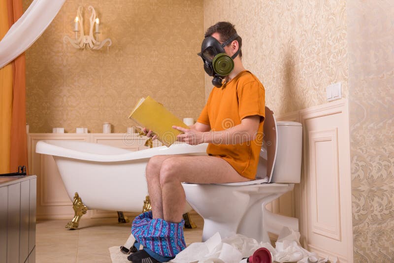 Man in gas mask sitting on toilet and reading book stock photo