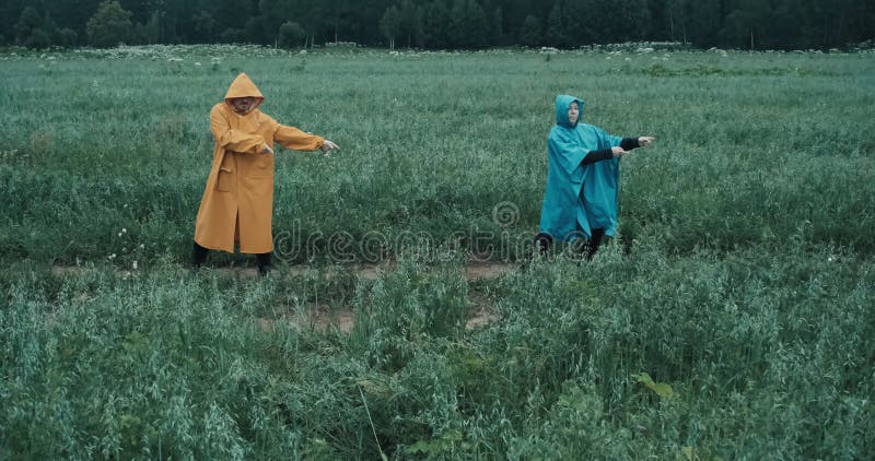 Man in gele regenjas en een vrouw in blauwe regenjas dansen in een veld