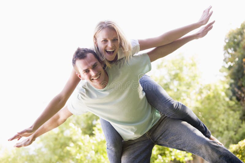 Man giving woman piggyback ride outdoors smiling. 