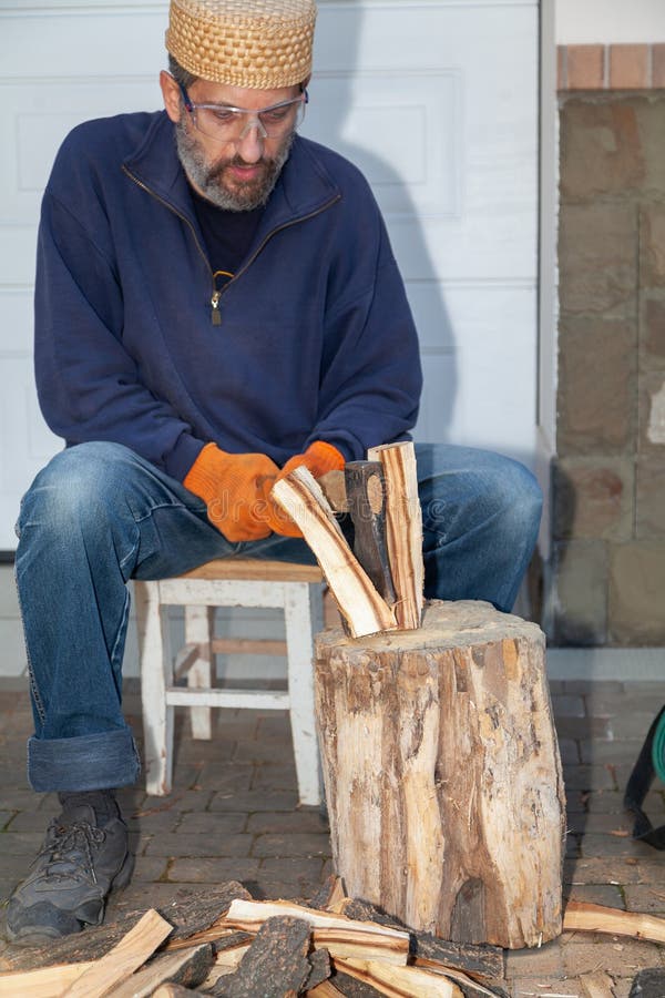 Man with glasses chopping wood in courtyard of house stock photo