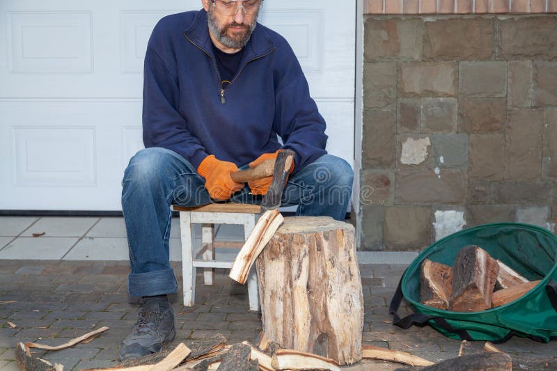 Man with glasses chopping wood in courtyard of house stock photo