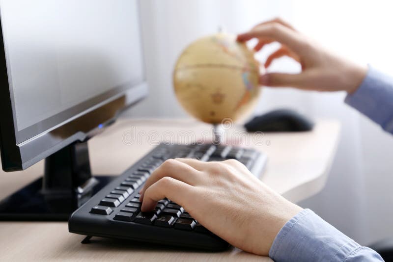 Man with globe sitting at PC keyboard. Concept of choosing travel tour royalty free stock photo