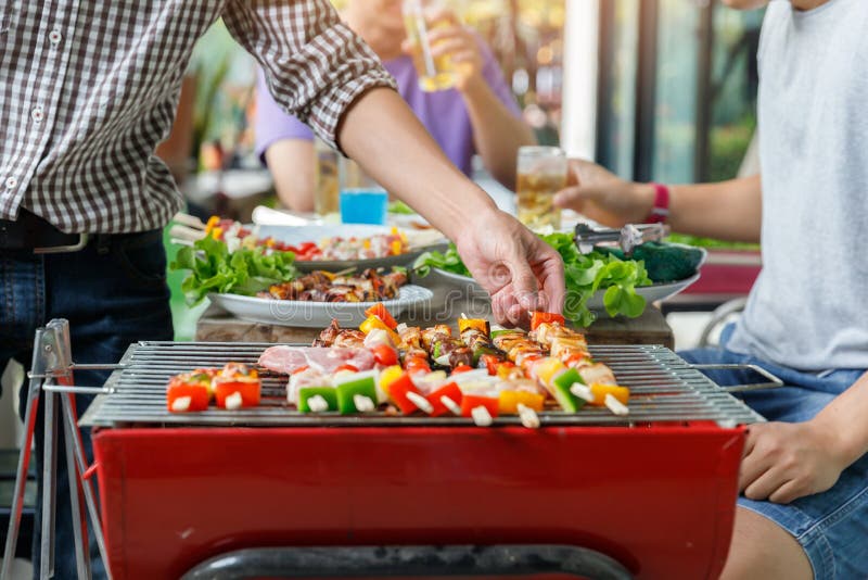 A man grilling pork and barbecue in dinner party. Food, people and family time concept